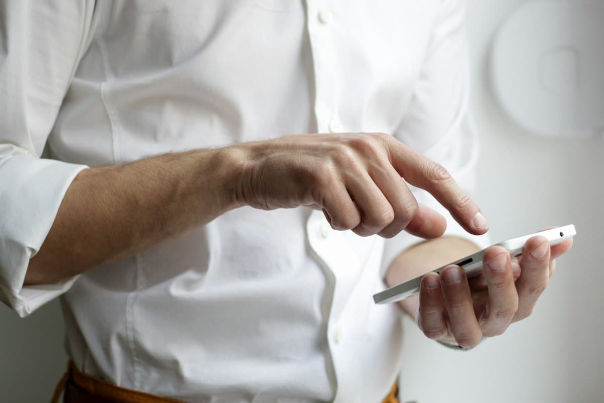 Une personne en chemise blanche consulte son téléphone.