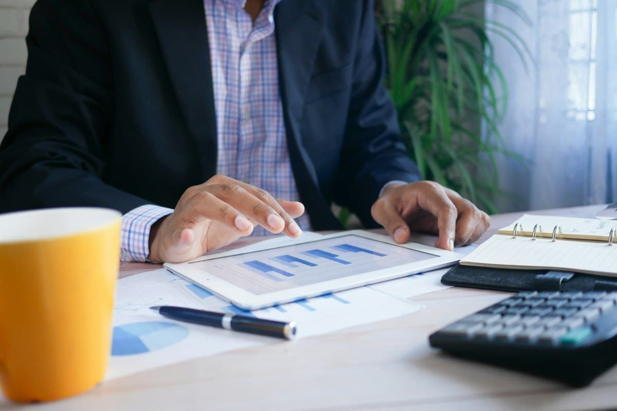 Une personne consulte un graphique sur une tablette, entre une calculatrice et des documents.
